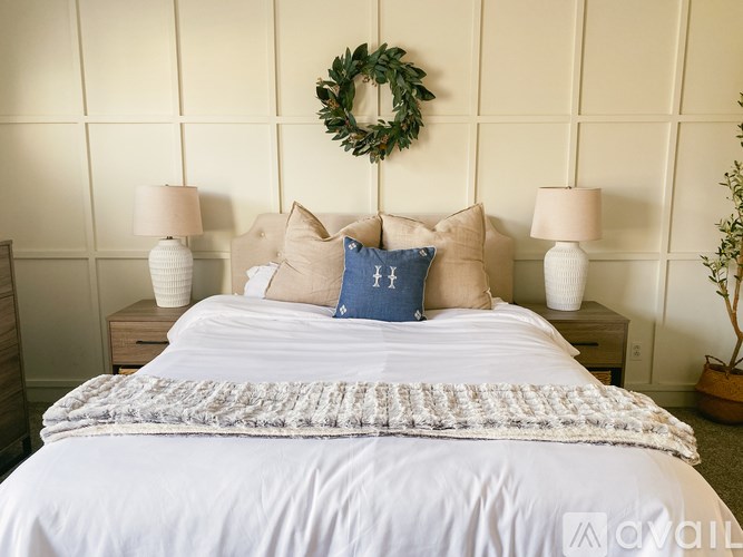 A bed with a white comforter and a blue pillow with a cross on it.