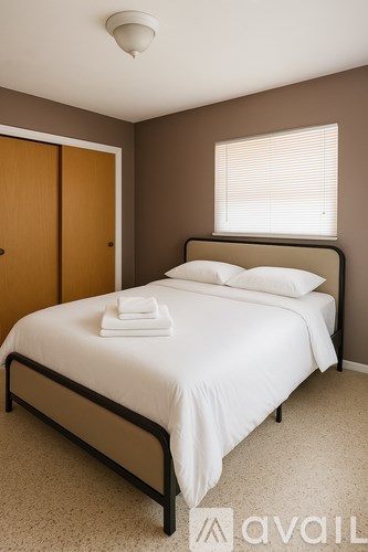 A bedroom with a white bed and a window with blinds.