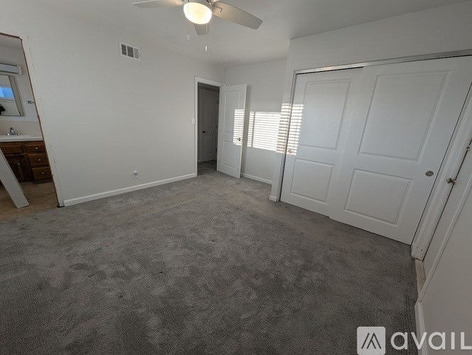 A spacious room with a carpeted floor, a ceiling fan, and a door leading to another room.