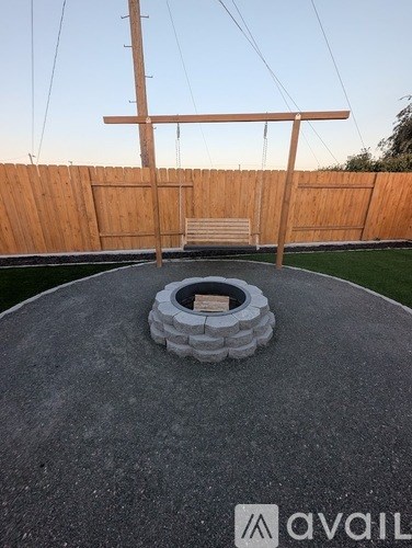 A circular stone structure sits in the middle of a concrete area with a wooden fence in the background.