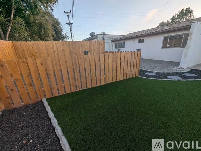 A backyard with a wooden fence and artificial grass.