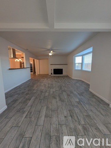 A spacious room with wooden flooring and a fireplace.