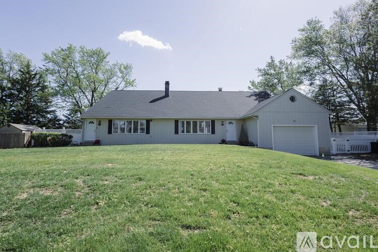 A large white house with a grey roof and a garage is surrounded by a green lawn.