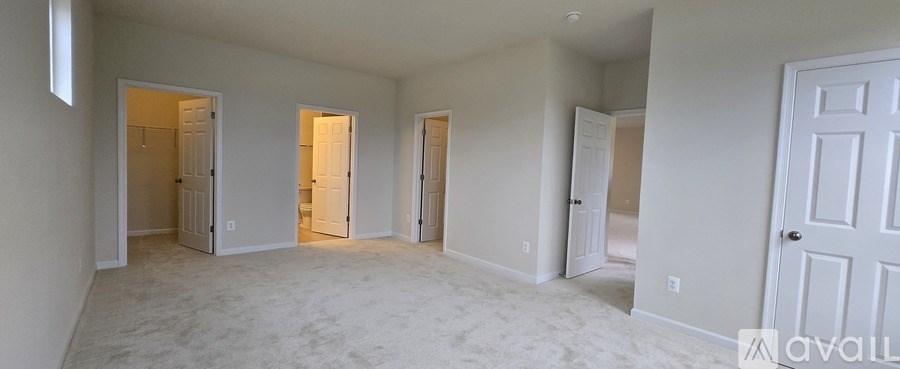 A room with white walls and carpeting, and a door on the right.