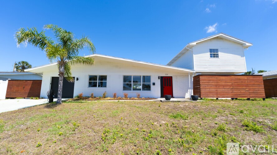 A white house with a red door and a palm tree in front.