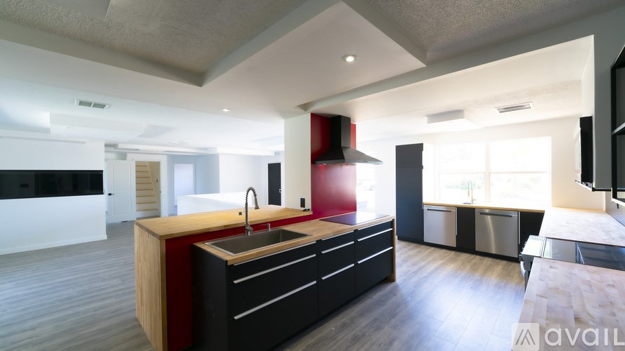 A modern kitchen with a red accent wall and black cabinets.