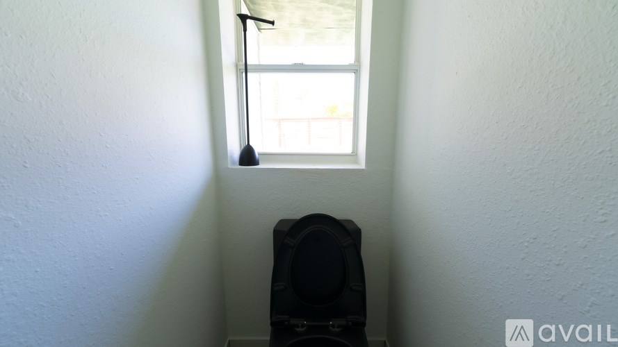 A black speaker is on a stand in a room with white walls and a window.