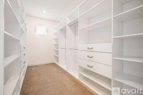 A walk-in closet with white shelving and drawers.