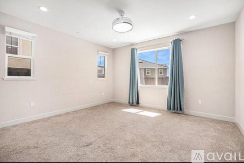 A room with a carpeted floor, a window with a view of a building, and a ceiling fan.