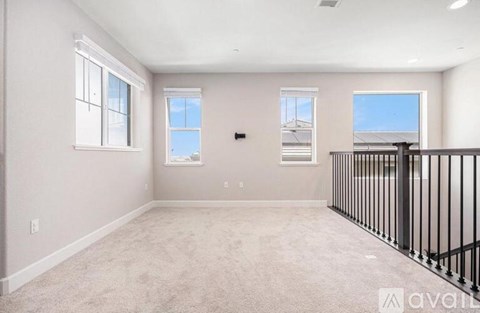 A spacious room with beige carpeting and a black railing on the balcony.