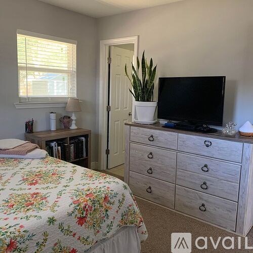 A bedroom with a floral bedspread, a white dresser, and a television on top of it.
