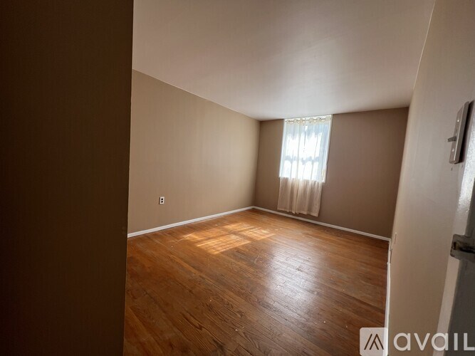 A room with wooden flooring and a window with white curtains.