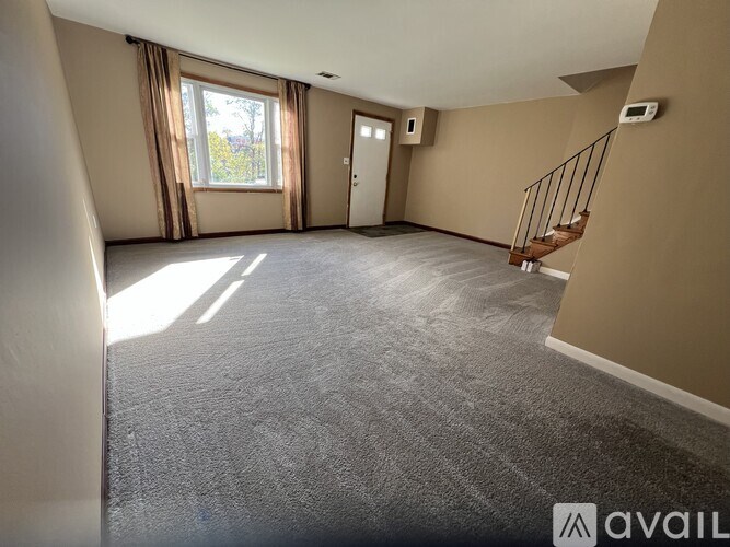 A spacious room with a carpeted floor, a staircase, and a window with curtains.
