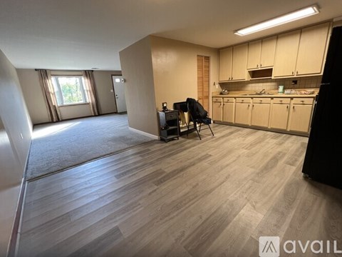 A spacious room with wooden flooring and a kitchen area with cabinets and a countertop.