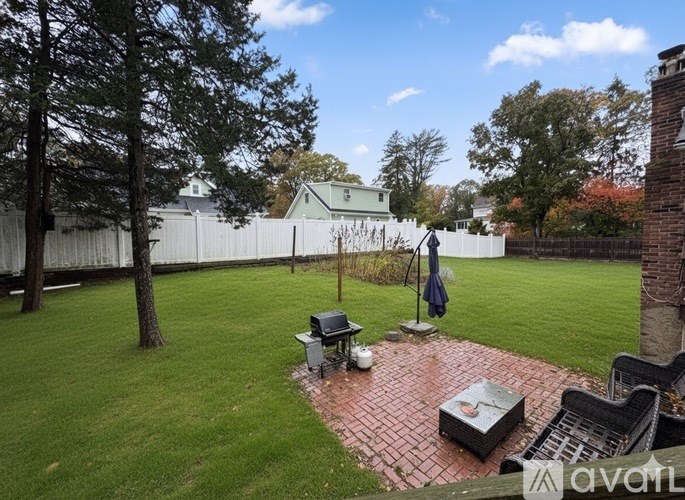 A backyard with a brick patio and a white fence.