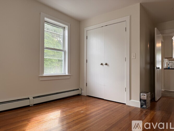 A room with a white door and a window with a view of greenery outside.