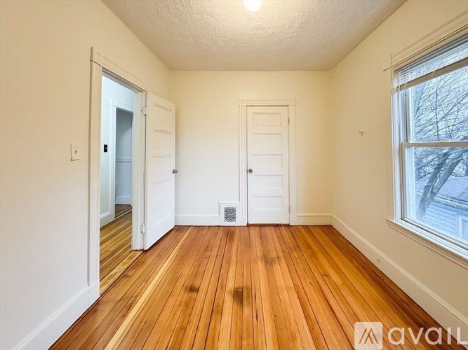 A room with wooden floors and white walls, with a window showing a tree outside.