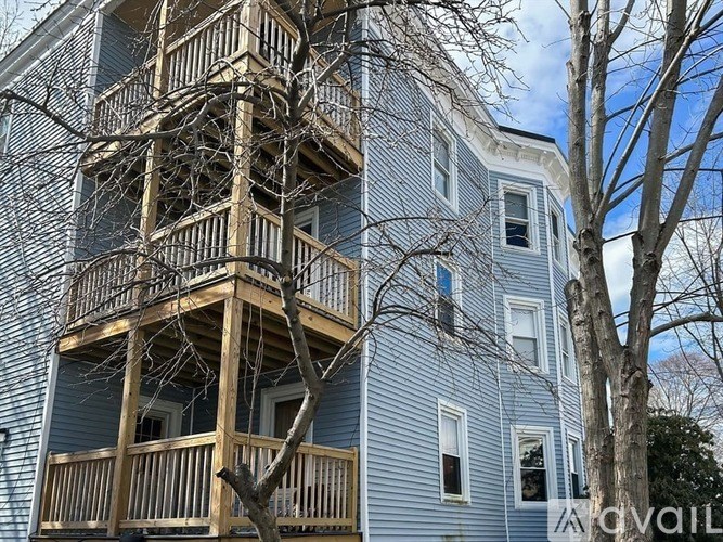 A tall apartment building with a balcony and a tree in front.