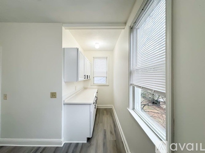 A kitchen with white cabinets and a window with blinds.