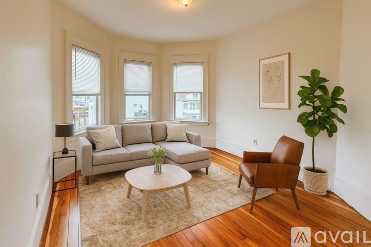 A living room with a grey couch, a brown chair, a white coffee table, and a plant.