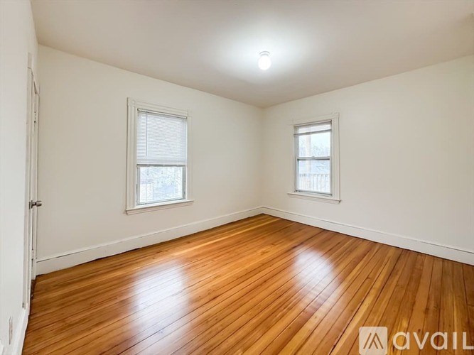 A room with wooden flooring and two windows.