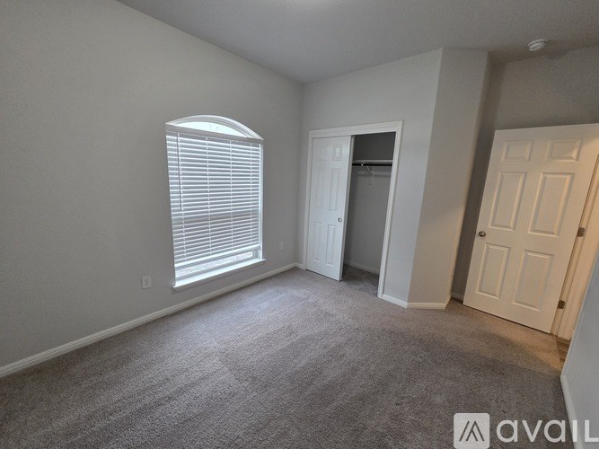 A room with a carpeted floor, a window with blinds, and a door leading to another room.