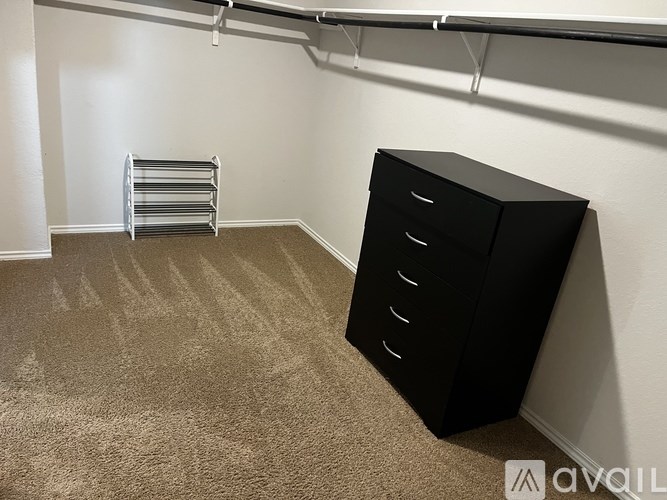 A black filing cabinet sits in a room with a carpeted floor and a metal rack in the corner.