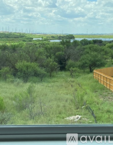 A view from a window looking out to a green landscape with a body of water and power lines in the distance.