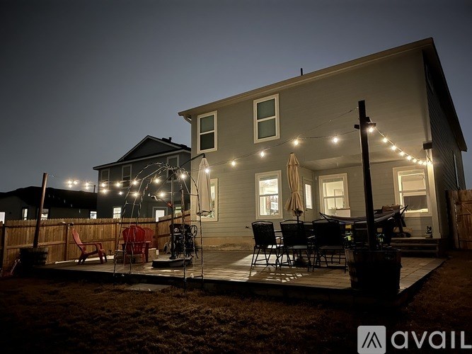 A house with a deck and patio furniture is lit up with string lights.