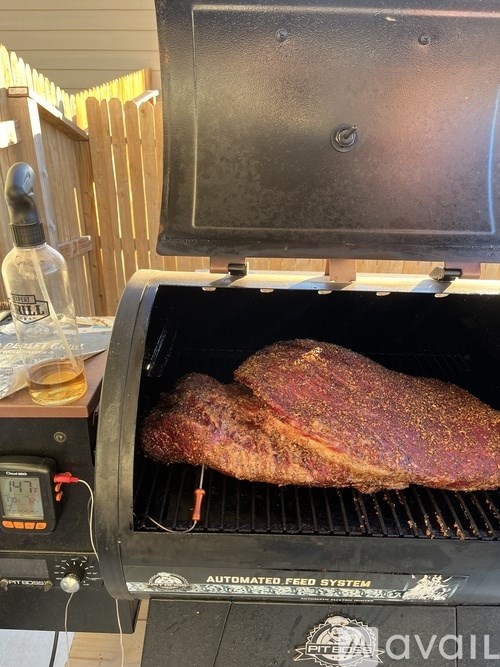 A large piece of meat is being cooked on a grill with a digital display and a bottle of sauce nearby.