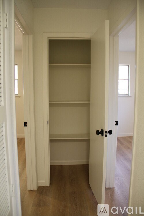 A white door with a black handle is open to a room with a white wall and a wooden floor.