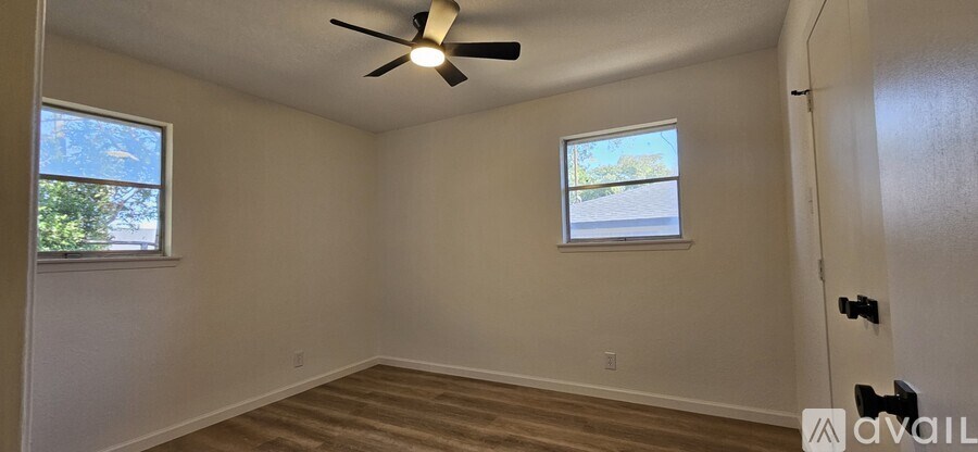 A room with a ceiling fan and two windows.
