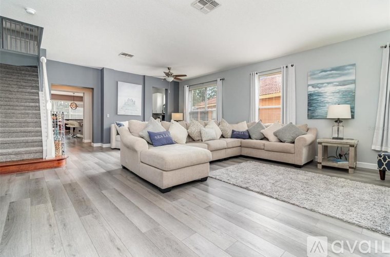A living room with a staircase on the left and a couch with multiple pillows in the center.