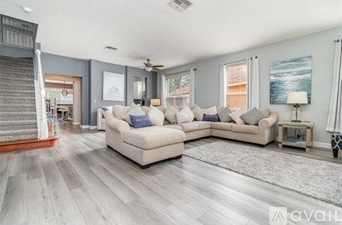 A living room with a staircase on the left and a couch with multiple pillows in the center.