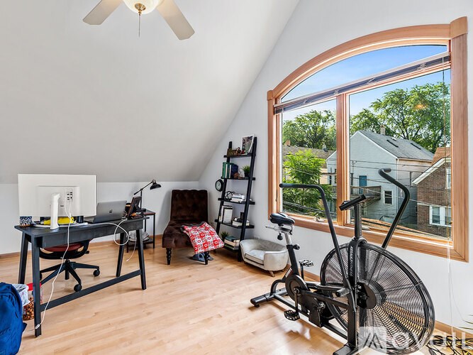 A room with a fan, a desk, a chair, a ladder, a yoga mat, and a bicycle.