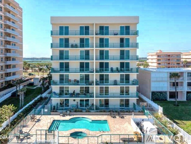 A large white apartment building with a pool in the foreground.