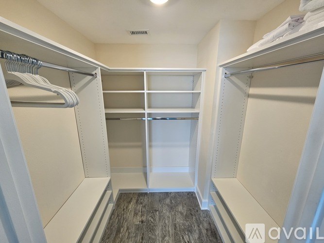 A walk-in closet with white shelves and a wooden floor.