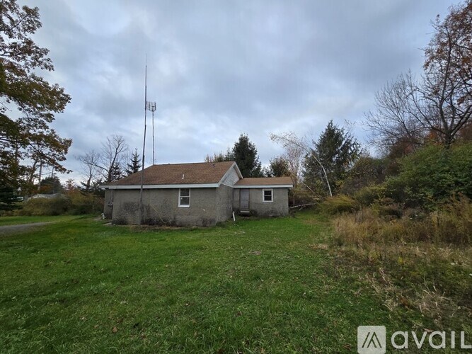 A small house with a tall antenna on the roof is situated in a grassy field.