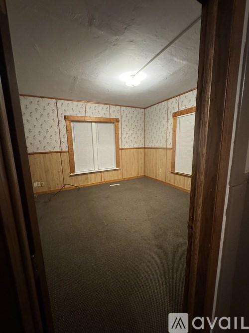 A room with a carpeted floor and two windows with wooden frames.