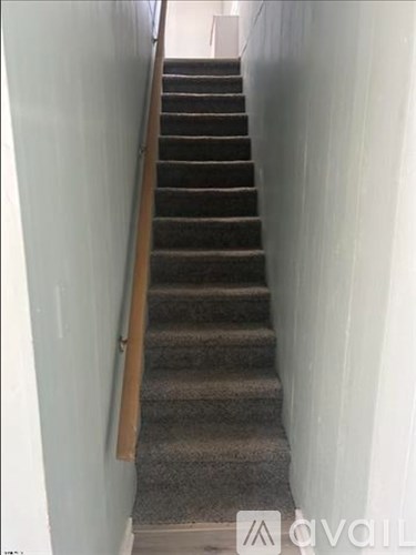 A staircase with a wooden handrail and carpeted steps.