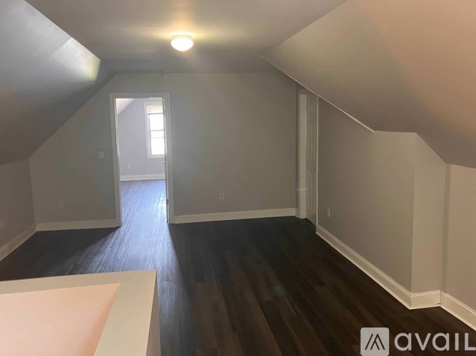 A room with wooden floors and white walls, with a window in the distance.