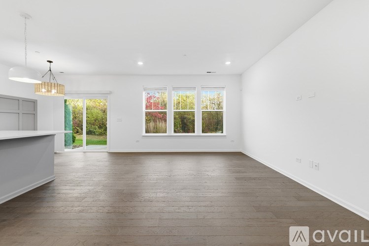 A spacious room with wooden flooring and a large window with a view of greenery outside.