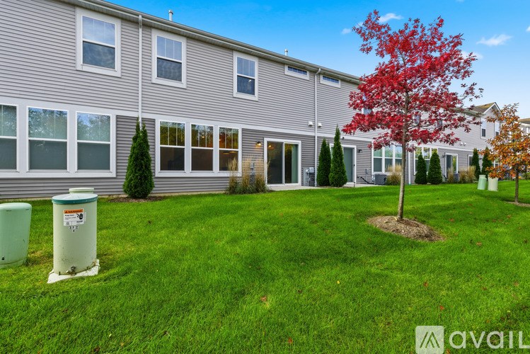 A tree with red leaves stands in front of a grey building.
