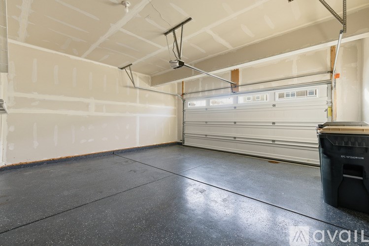A large empty garage with a black trash bin on the floor.