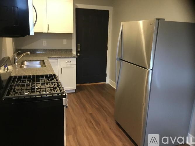 A kitchen with a black stove top oven, a black microwave, a black refrigerator, and a stainless steel refrigerator.