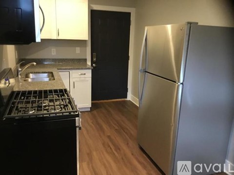 A kitchen with a black stove top oven, a black microwave, a black refrigerator, and a stainless steel refrigerator.