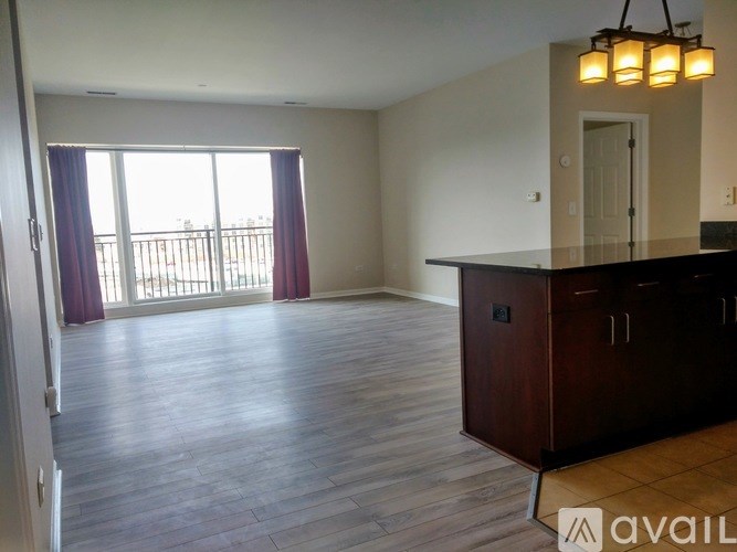 A spacious room with wooden flooring and a large window with curtains.