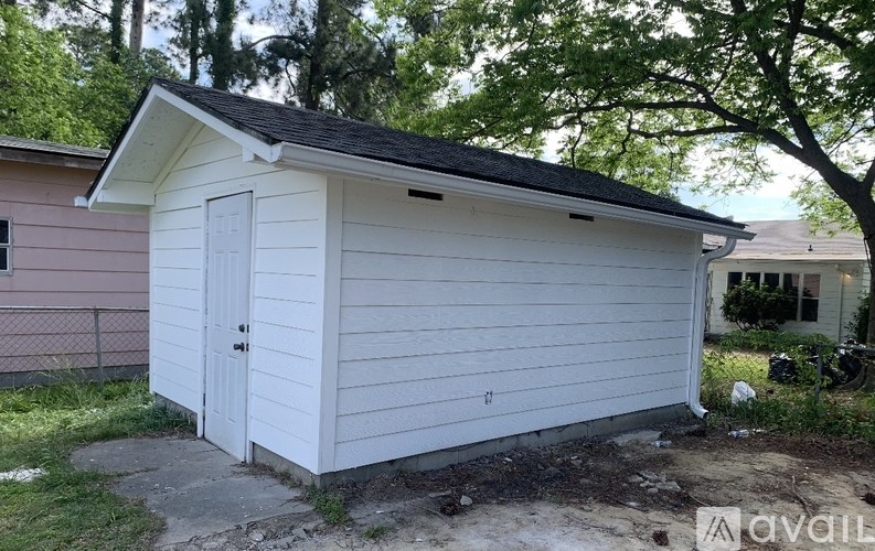 A small white shed with a black roof sits in a yard.
