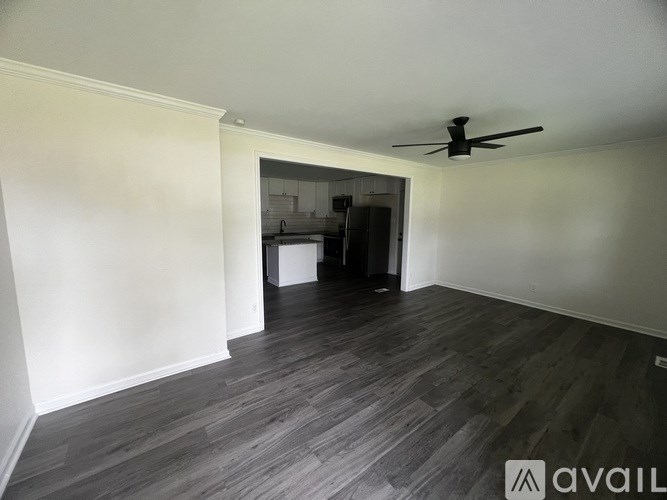 A room with a ceiling fan and a view of a kitchen through a doorway.