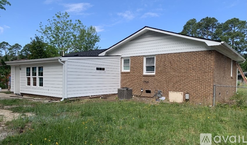 A house with a white siding and a brick wall is surrounded by grass and trees.